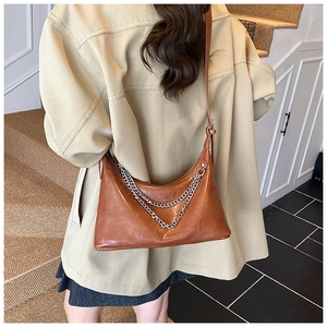Detail of a brown shoulder bag with double silver metal chains worn over a beige coat