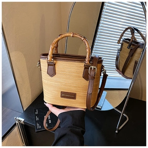 Detail of woven straw bucket bag featuring bamboo handle and adjustable leather strap