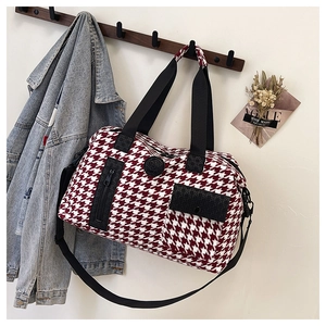 Detail of red houndstooth travel bag with black straps hanging on a wooden hook