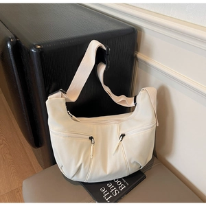 Close-up of minimalist cream white dumpling bag with dual zipper pockets and adjustable strap