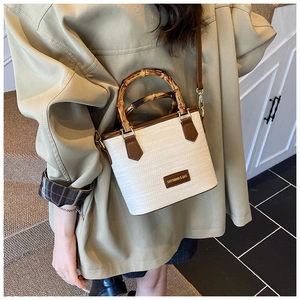 Detail of woven bucket bag featuring bamboo handles and brown leather trim accents