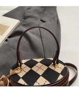Detail of a brown leather cylinder bag with knit argyle pattern and gold-tone metal hardware