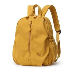 Detail of mustard yellow nylon backpack featuring a metal logo and vertical zipper pocket