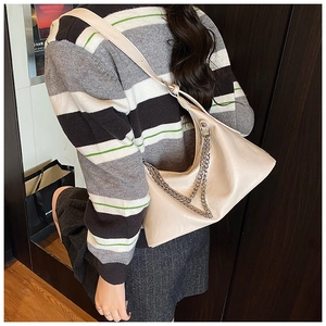 Detail view of beige leather dumpling bag with silver chain straps worn by a model