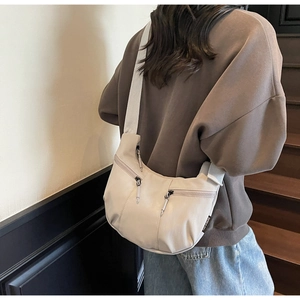 Detailed view of beige crescent bag with zipper pockets and wide shoulder strap