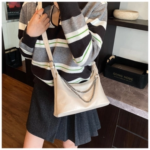 Close-up of cream shoulder bag featuring silver chain detail and adjustable strap
