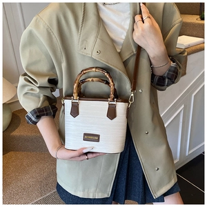 Detail of hand-woven bucket bag with bamboo handle and brown leather trim on stairs