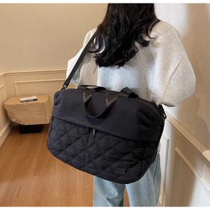 Detail of black quilted nylon travel bag with diamond stitching and adjustable strap