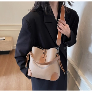 Chic beige and brown pebbled leather bucket bag with wide strap worn by a model