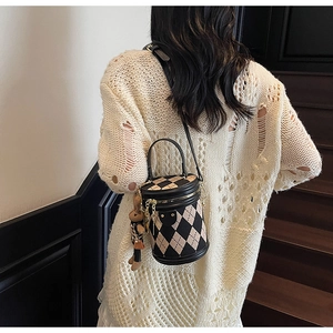 Quilted cylinder bag with brown bear charm shown on a model by a wooden staircase