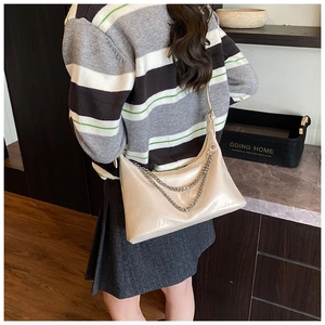 Detail of cream glossy shoulder bag with double silver chain straps on female model