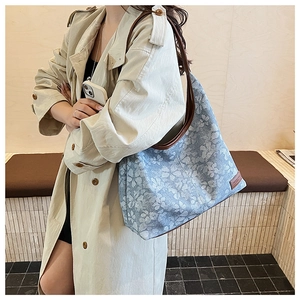 Detail of floral hobo bag with brown leather strap worn over a beige trench coat