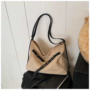 Detail of hobo bag with beige suede texture, black strap and gold metal eyelets