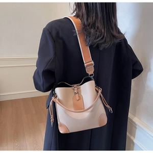 Rear view of a model wearing the beige bucket bag with wide woven strap and brown leather accents