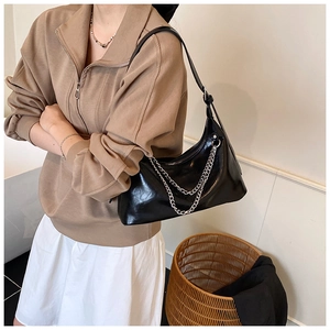 Detail of glossy black leather shoulder bag with decorative silver chains for women