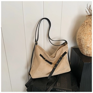 Detail of beige suede tote bag featuring black decorative straps and gold metal buckles