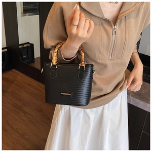 Detailed view of woven black bucket bag featuring natural bamboo handle and gold hardware
