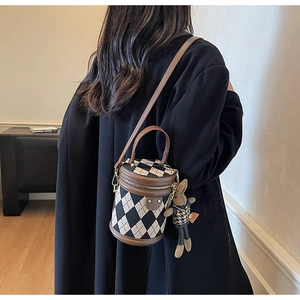 Quilted cylinder crossbody bag with bunny charm shown on model in stylish indoor setting