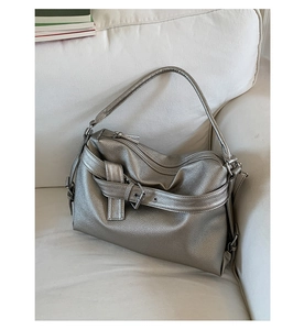 Detail of silver metallic pebbled leather tote bag with buckle straps on a white sofa