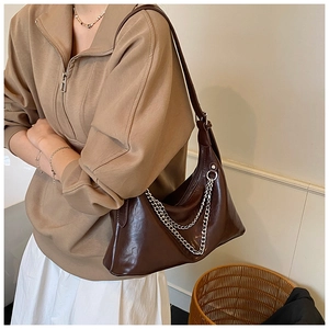 Detail of dark brown leather shoulder bag with silver double chain accents and smooth texture