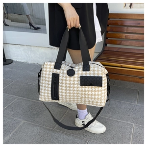 Detail shot of houndstooth travel bag with black straps and logo on outdoor bench
