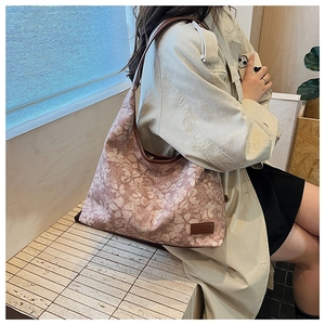 Detailed view of pink floral canvas tote with brown leather strap and brand patch