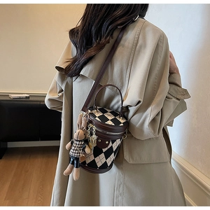 Detail of checkered bucket bag with leather trim and plush bunny charm on a model
