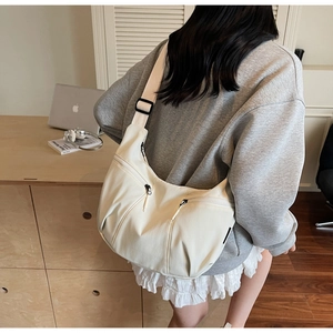 Close-up of cream white dumpling crossbody bag with two front zippers and wide strap