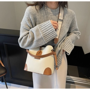Detail of cream bucket bag with brown leather trim and wide canvas shoulder strap