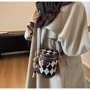 Detail of checkered cylinder bag with leather handle and plush bunny charm on a model