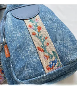Detail of light blue denim crossbody bag with colorful ethnic floral embroidered strap