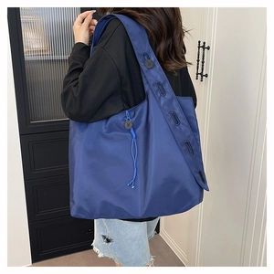 Side view of a large navy nylon tote bag with drawstring details and wide shoulder strap