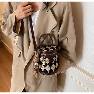 Cylindrical bucket bag with beige and black diamond patterns and a plush rabbit charm