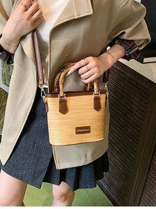Summer straw bucket bag with bamboo handle and brown leather trim worn by model