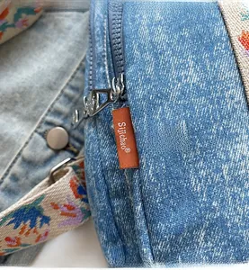 Close-up of denim fabric with orange woven label and floral embroidered shoulder strap