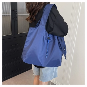 Macro detail of foldable blue nylon tote bag showing wide strap and side buckle