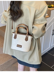 Straw woven bucket bag with bamboo handles and leather trim shown in a crossbody style
