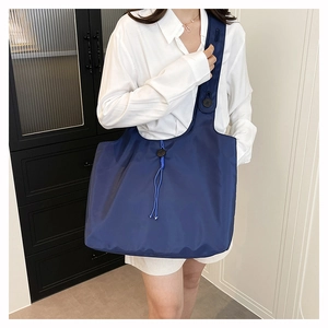 Detail of navy blue nylon tote bag with drawstring, button details and wide shoulder strap