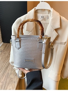Silver woven crossbody bucket bag with dark brown bamboo handle and adjustable shoulder strap