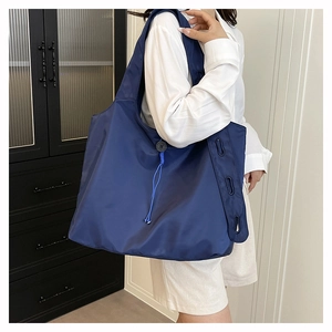 Detail of dark blue nylon tote bag showing drawstring buckle and decorative side eyelets