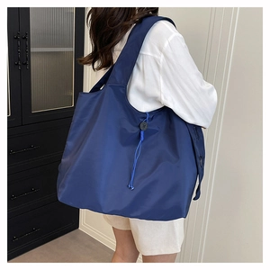 Detail view of large navy nylon tote bag with drawstring and button accents on a model