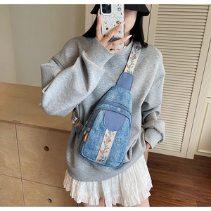 Detail of blue denim sling bag featuring vibrant floral embroidered wide shoulder strap