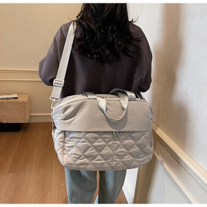 Detailed back view of a light gray quilted nylon travel bag on a female model