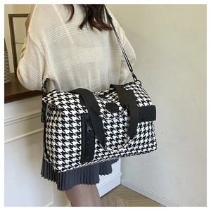 Side view of a large black and white houndstooth travel bag worn by a model