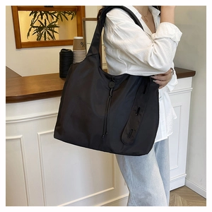 Detail of a large black nylon tote bag with drawstring and side straps in a cafe setting