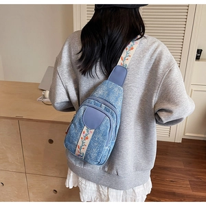 Detailed embroidery on a light blue denim crossbody chest bag with floral strap details