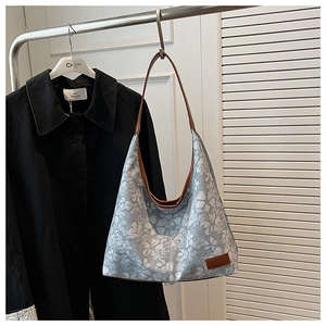 Close-up of light blue floral tote bag with brown leather trim on shop display