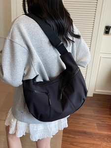 Versatile black crescent dumpling bag with multiple pockets worn by model in home setting