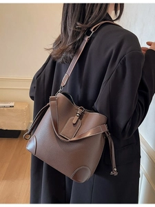 Deep brown pebble leather bucket bag with woven strap shown on a model in a modern interior