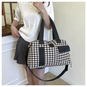 Detail of large houndstooth travel bag with black leather handles and crossbody strap
